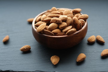 Almonds nut close-up.Raw almonds in a round wooden cup on a black slate background. Nuts in a cup.Vegetarian and vegan food.
