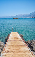 Wooden dock on Mediterranean Sea and sailing boat in background.