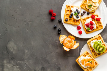 Fototapeta na wymiar Beautiful yummy snacks. Waffles with cream and friuits on grey background top-down frame copy space