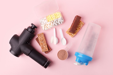Therapeutic percussive massage gun, fit meal, pills, sport energy bar on pink background - concept...