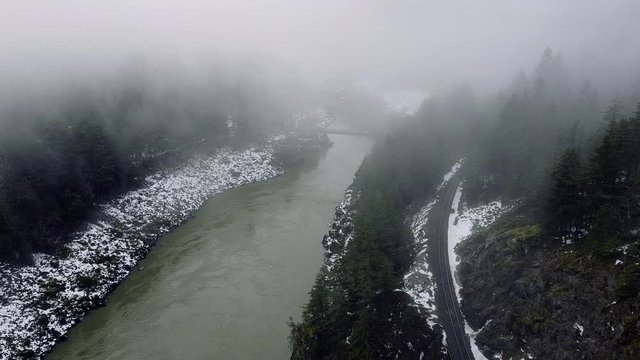 Aerial view of slow moving river covere with the clouds, railroad and the mountain with the green forest trees