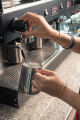 close-up woman barista in apron preparing and pouring milk into hot cup in coffee shop