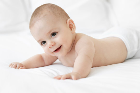 Cute baby in diaper lying on white bed bending head