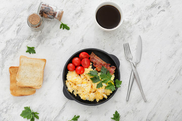 Frying pan with scrambled egg, bacon and tomatoes on white background