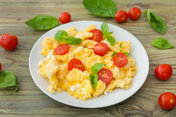 Tasty scrambled eggs with tomatoes and basil on plate