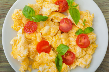 Tasty scrambled eggs with tomatoes and basil on plate