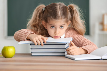 Cute little schoolgirl with books at desk in classroom