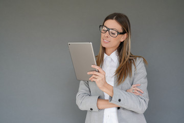 Businesswoman standing on grey background and using tablet, isolated