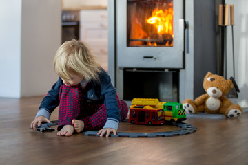 Obraz premium Toddler boy, playing with train and railway in front of the fireplays in pajama