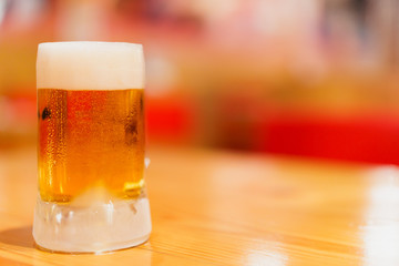 mug of cold draft beer on wooden table with blurred red and yellow background, selective focus
