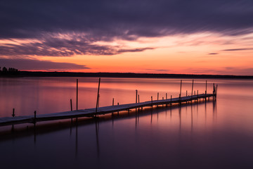 Naklejka na ściany i meble Dramatic sky over a idyllic lake with a long wooden jetty, Sweden.