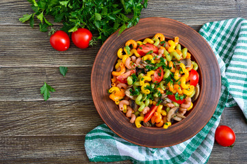 Tasty warm salad. Colored pasta with mushrooms and fresh tomatoes in a bowl on a wooden table. Pasta colorata. The top view