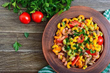 Tasty warm salad. Colored pasta with mushrooms and fresh tomatoes in a bowl on a wooden table. Pasta colorata. The top view