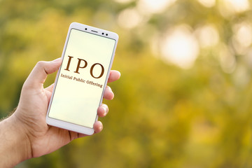 IPO Background Concept. Initial Public Offering concept. Young male hand holding mobile phone &...