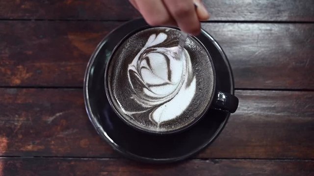 Top view of person hand stirring Goth latte coffee with spoon. The black colour is caused by adding activated charcoal to espresso and then adding milk.
