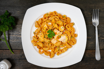 Macaroni in tomato sauce with sausage and fried egg in white dish on wooden table.