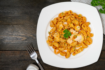 Macaroni in tomato sauce with sausage and fried egg in white dish on wooden table.