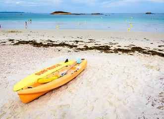 Lifeguards yellow rescue surfboard and sea kayak lying on a sandy beach at low tide in Penvenan, northern Brittany, France.