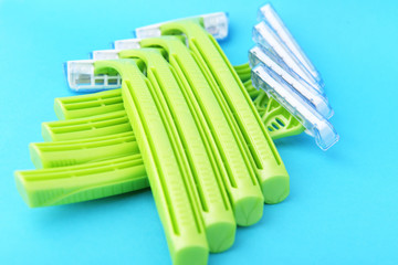 Green plastic disposable razor on a blue background. Safe shaving with sharp razor of female skin. Hair removal from the legs and face. Body care and beauty of a woman.