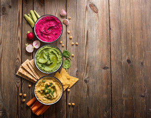 Various hummus dips on wooden background