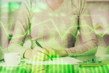 Hand taking notes in notepad. Forex chart holograms in front. Concept of research. Double exposure