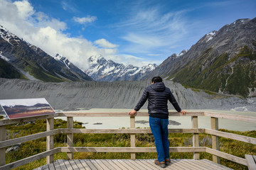 Fototapeta na wymiar A man tourist is watching Panorama view the mueller glacier and mueller lake at kea point in Mount Cook National Park, the rocky mountains and green grasses of summer in New Zealand.
