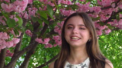 Young girl with beautiful make-up stands under a tree with bright pink sakura flowers