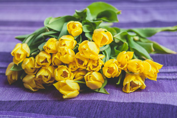 Flower bouquet of yellow tulips lying on purple background  tablecloth