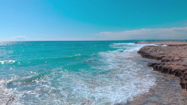 flight over the sea seashore, aerial drone view of waves crashing at rocky cliff with splashing and white foam, view of stones in blue water, cyprus Aya Napa