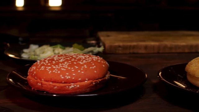 Burger buns on plates standing on wooden table in dark room before coooking process. Stock footage. Black and white burger buns with sesame seeds.