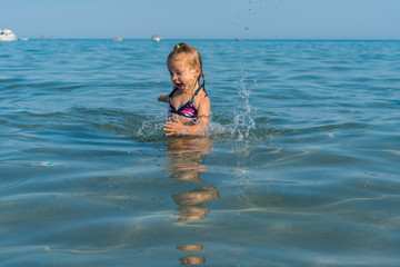a little girl enthusiastically jumps into the sea and laughs, splashes fly around her. summer...