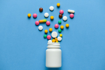 Assorted medicine pills, tablets, capsules blow out or ejection from bottle on blue background. Copy space for text - concept of medication treatment, health care