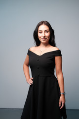 A large portrait of a middle-aged woman (30-35 years old) with dark hair and brown eyes in a black dress on a light background.