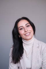 Portrait of a smiling mid-aged business woman in a light milk-colored trouser suit and turtleneck against a light wall.