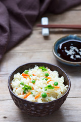Vegetarian rice dish with vegetables and green peas on a wooden background.