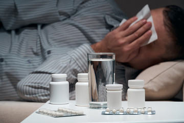 Overworked businessman is lying on the sofa and resting. Pills and glass of water near him.
