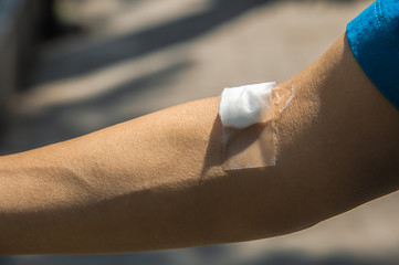 Closeup cotton ball with clear plaster on right arm after taking blood sample from hospital