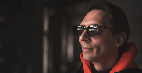 man in sunglasses looks away, closeup on a dark background