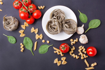 White plate with pasta with spinach, cherry tomatoes and baby spinach leaves on a gray background....