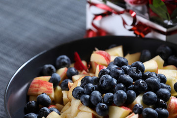 Fruit salad on a dark plate with red roses bouquet on the background