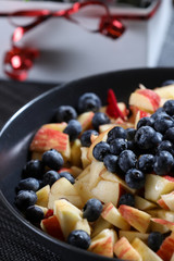 Fruit salad on a dark plate with red roses bouquet on the background