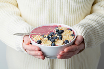 Berry smoothie bowl in hands of female wearing white sweater. 