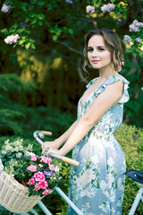 portrait of a beautiful girl in the forest, holding a bike with a basket of flowers, behind the rays of the sun, a blue flowered dress, summer walk