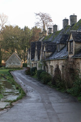 beautiful village in the English countryside, the houses are made of stone with dark roofs, abundant vegetation and trees in the background, bordered by a stream