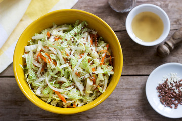 Coleslaw of cabbage, carrots and various herbs with mayonnaise in a large plate on a wooden background.