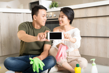 Happy young Asian couple showing smartphone while cleaning house.