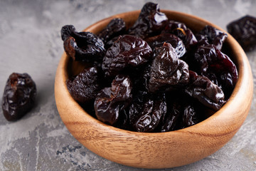 prunes, dried plums in a wooden bowl on a gray background Rustic style