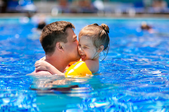 dad and daughter play and cuddle in the pool.