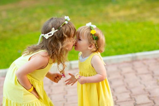 Two sisters in flower wreaths, yellow dresses kiss