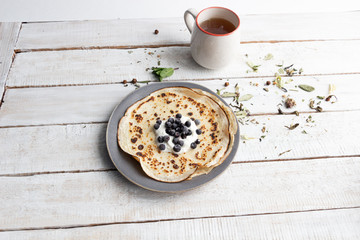 Pancakes with sour cream and blueberries on plate with cup of herbal tea on wooden background